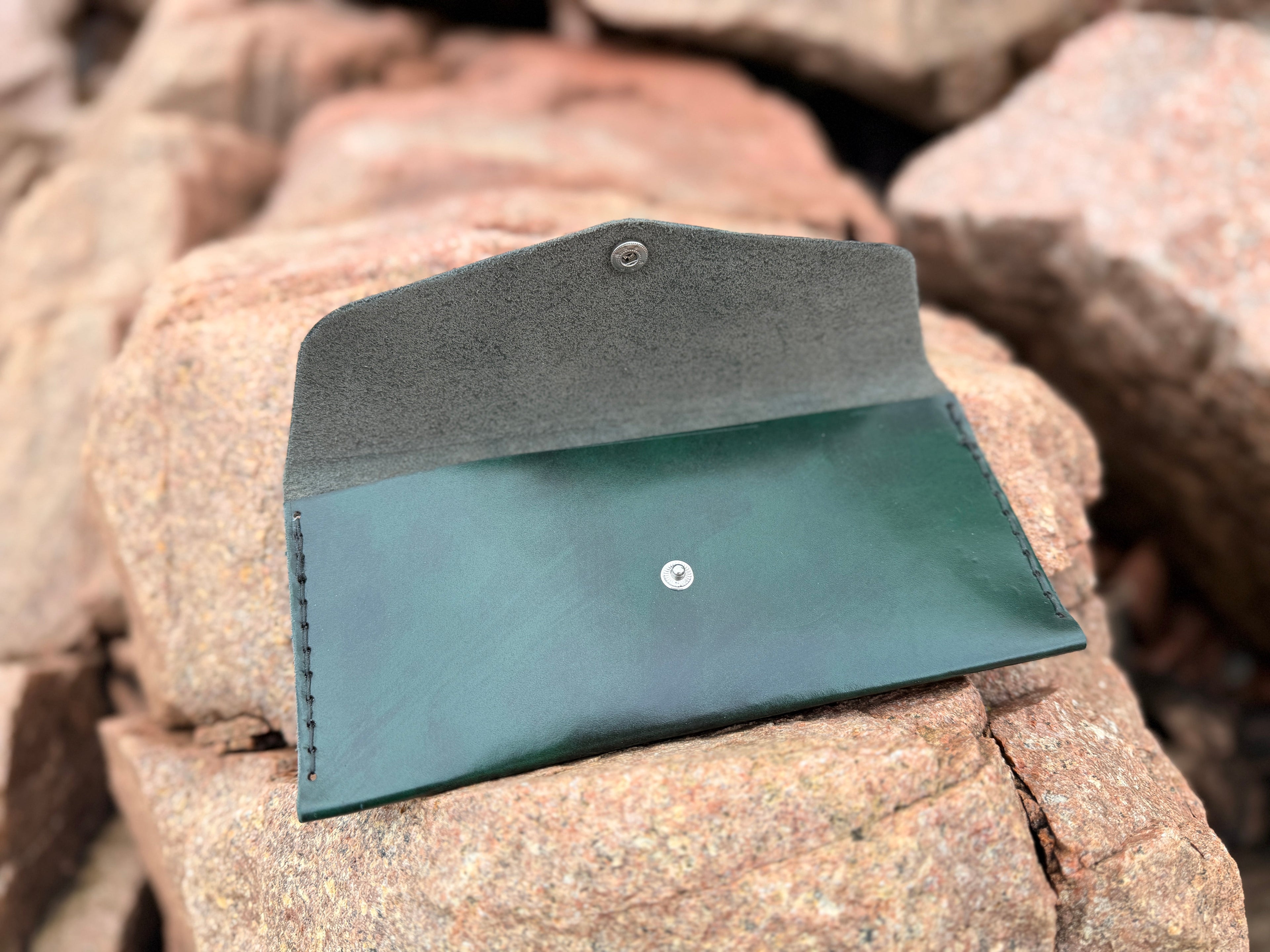 Forest green leather envelope wallet flat on stone