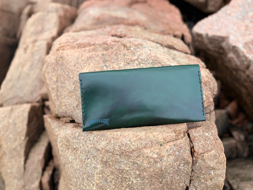 Forest green leather long wallet closed on Maine rocks