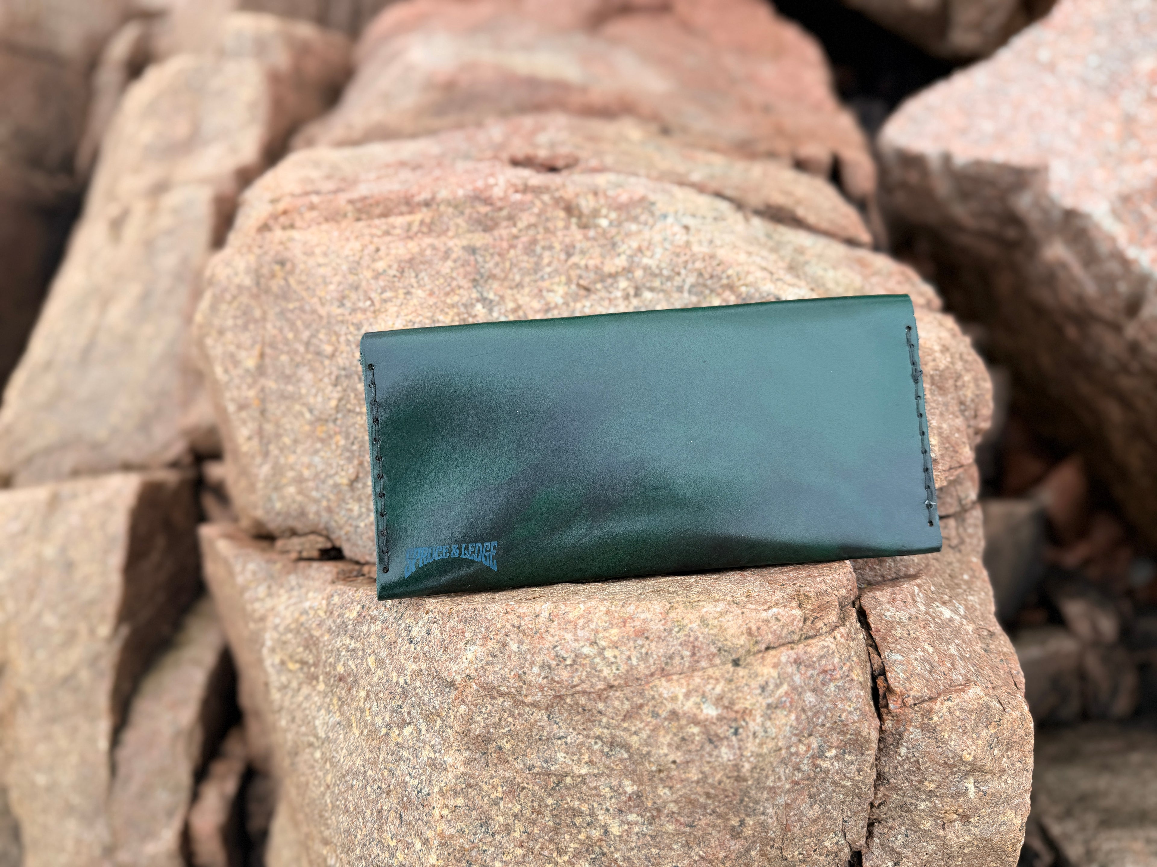 Forest green leather long wallet closed on Maine rocks